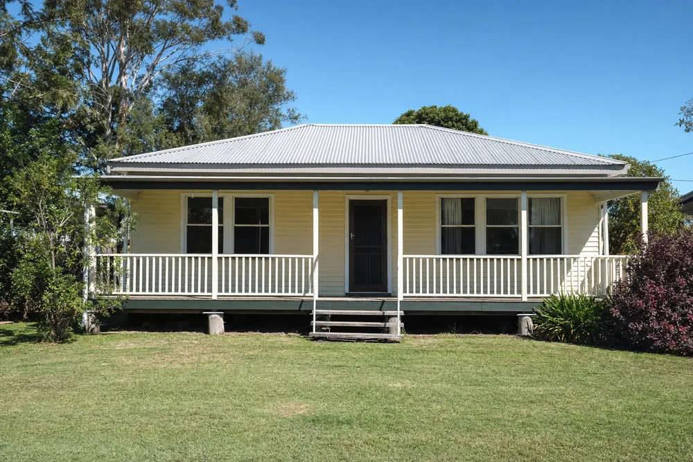 The front verandah of a single-storey timber-clad house with a steel roof, timber posts on short timber stumps and a white balustrade — restumping, Gold Coast. Illustrative example.